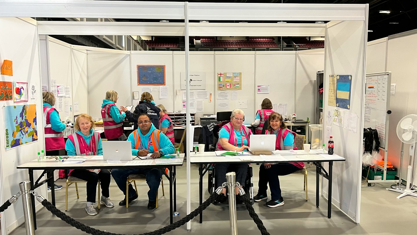 Freiwillige bedienen einen Infostand und arbeiten dabei an Laptops.